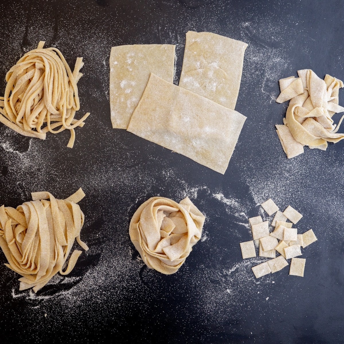 Different types of pasta on a black board.
