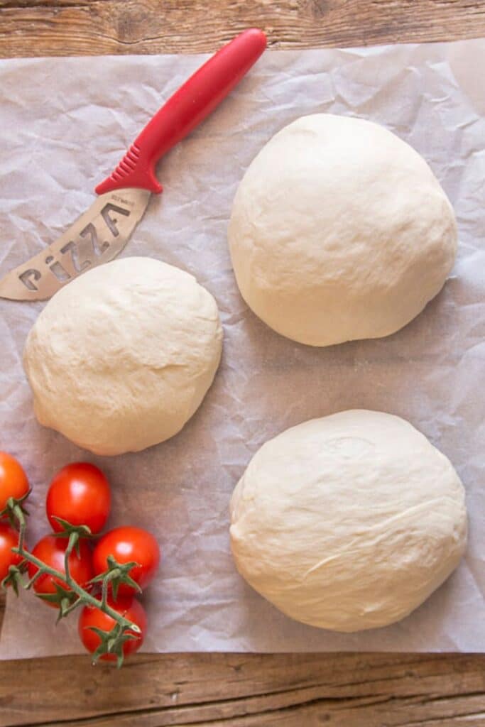Three pizza doughs on a parchment paper.