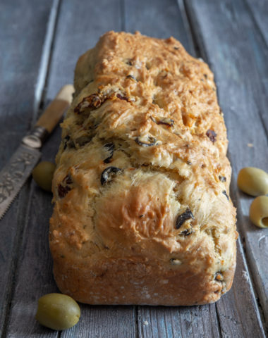 olive bread with olives and a knife on a blue board.