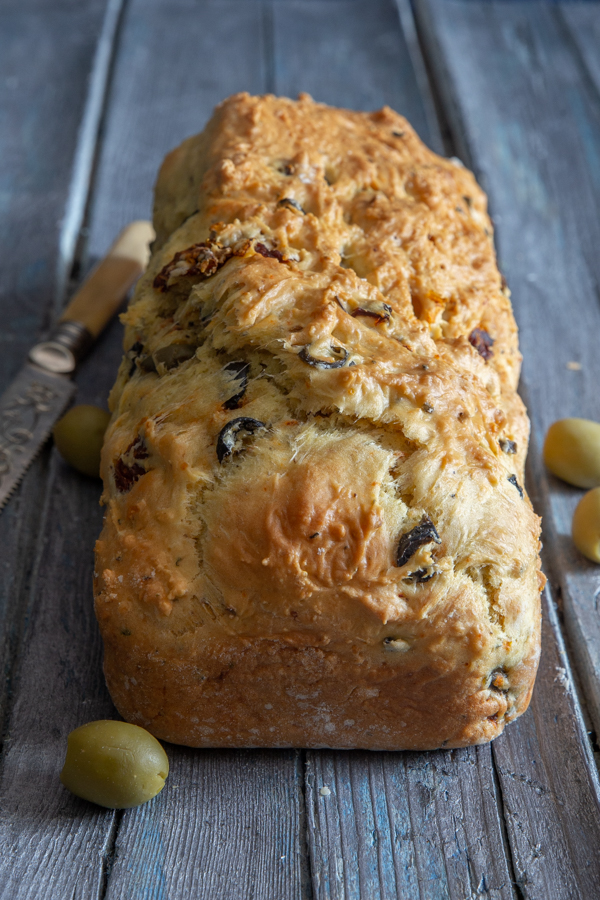olive bread with olives and a knife on a blue board.