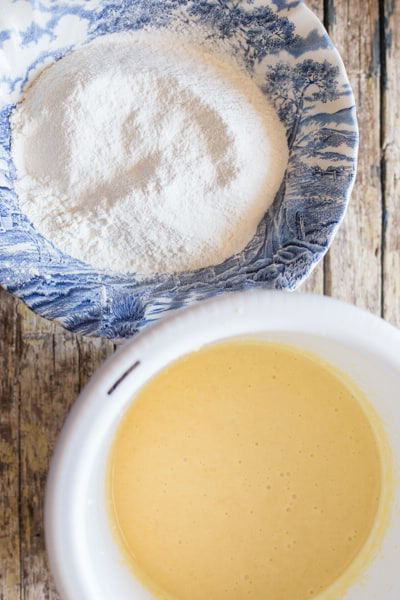 Beaten ingredients in a white bowl and whisked dry ingredients in a blue bowl.