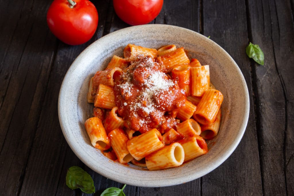 Pasta with sauce in a silver bowl with grated parmesan cheese on top.