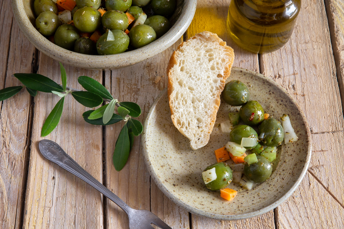 olives in a grey bowl, some olive salad & a slice of bread on a grey plate.