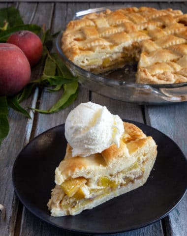 peach pie in a glass dish with a slice & a scoop of ice cream on a black plate.
