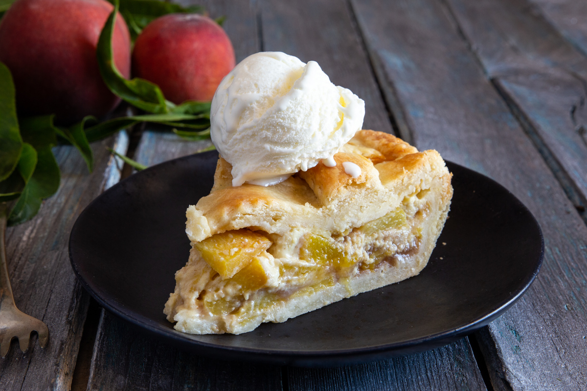 A slice of pie on a black plate with a scoop of ice cream.