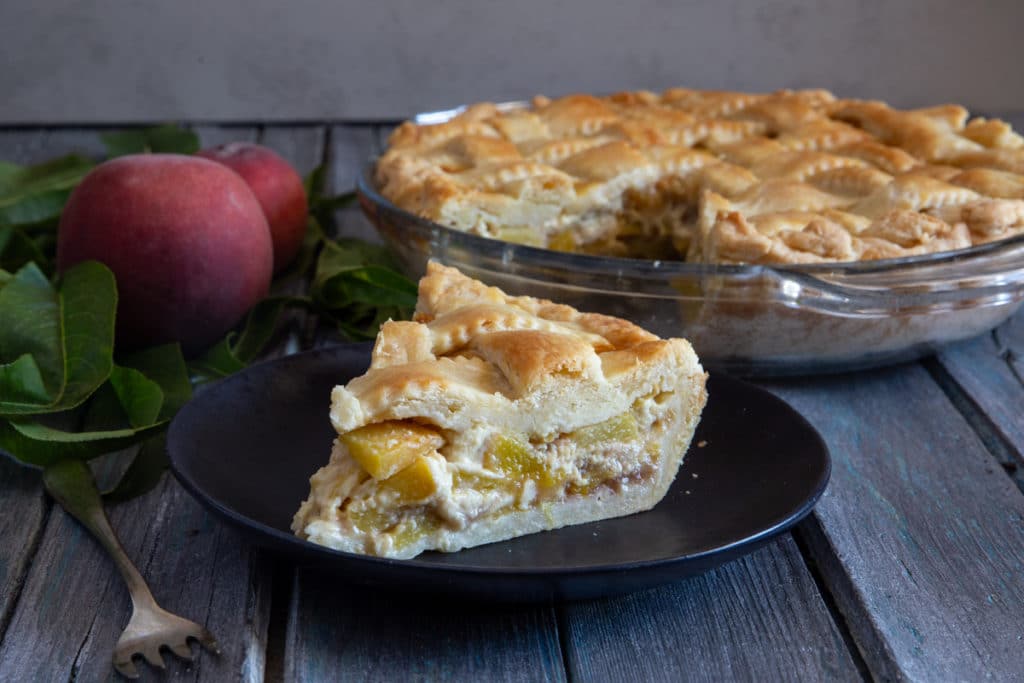 peach pie in a glass dish with a slice on a black plate.