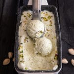 Pistachio ice cream in a white loaf pan with 2 scoops on top.