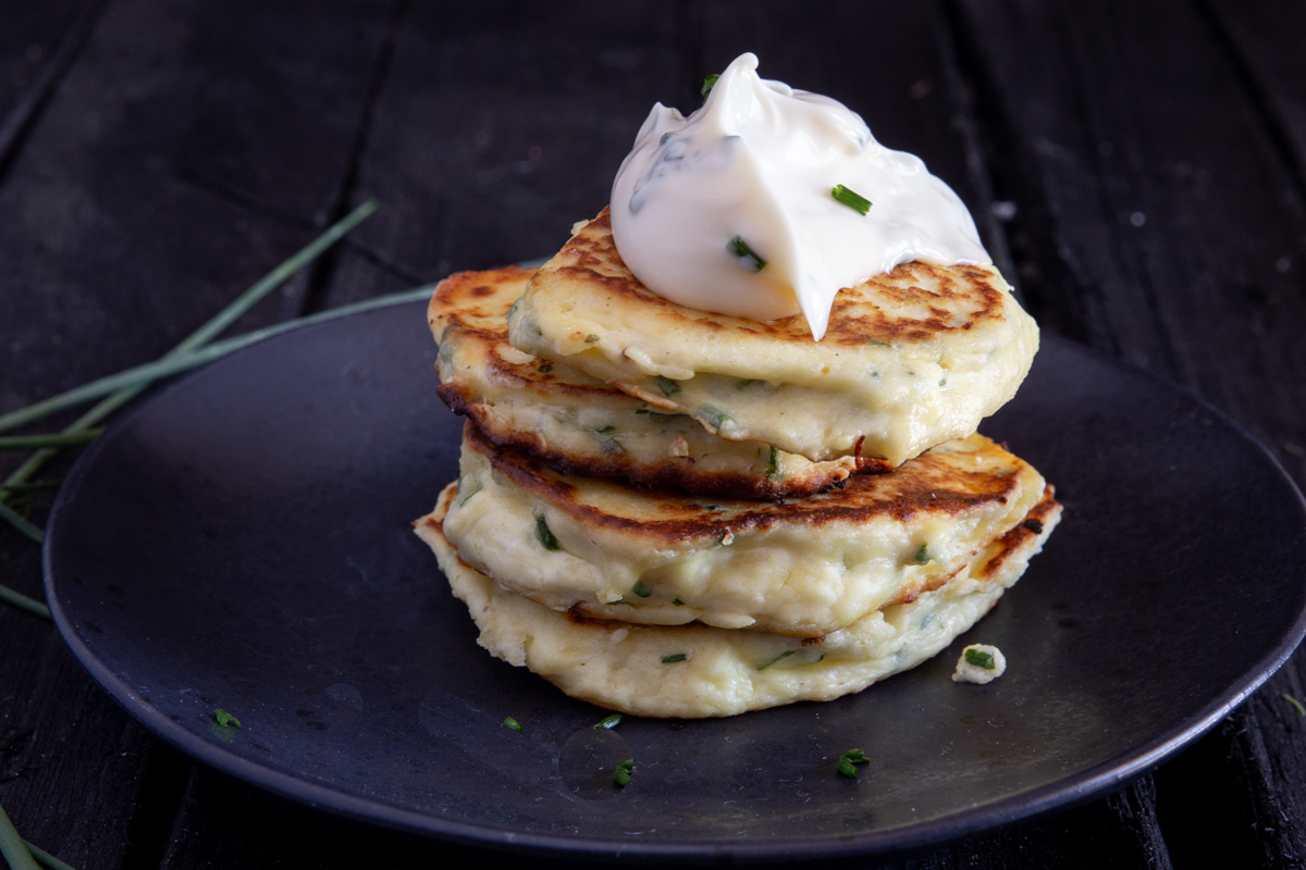 4 stacked fritters on a black plate with a dollop of chive mayo on top.