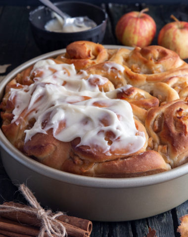Apple cinnamon rolls in a baking pan, half frosted.
