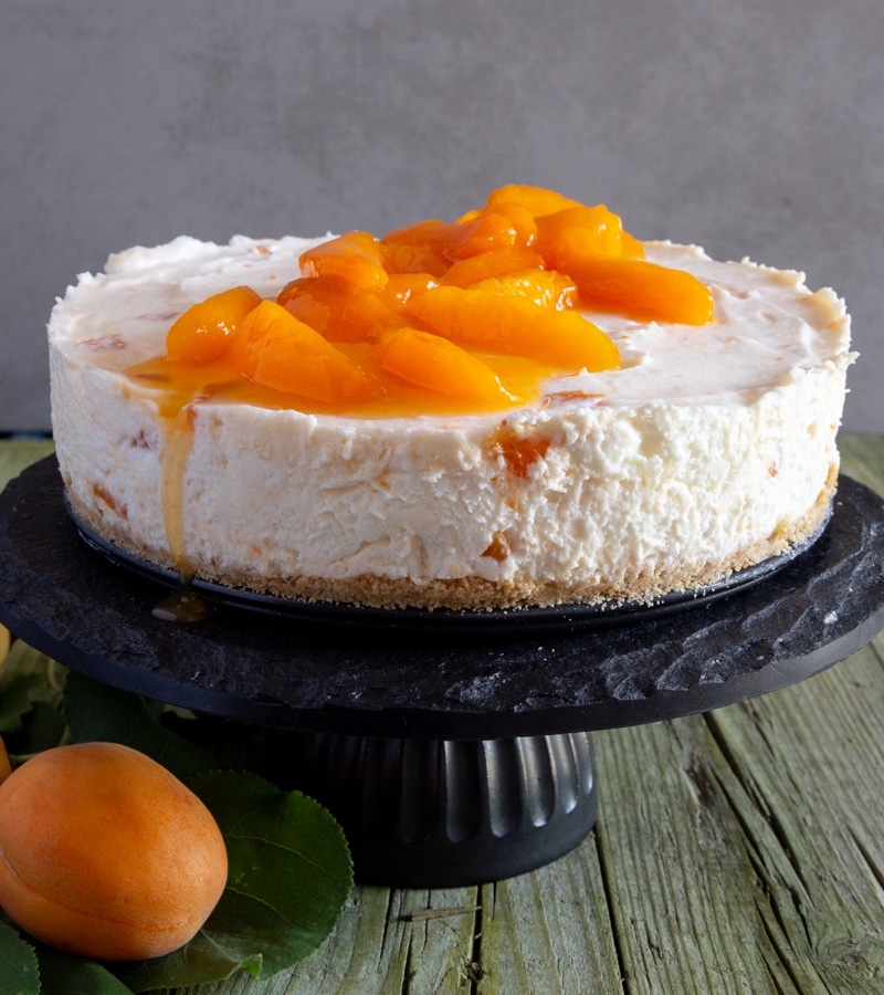 Apricot cheesecake on a black cake stand.