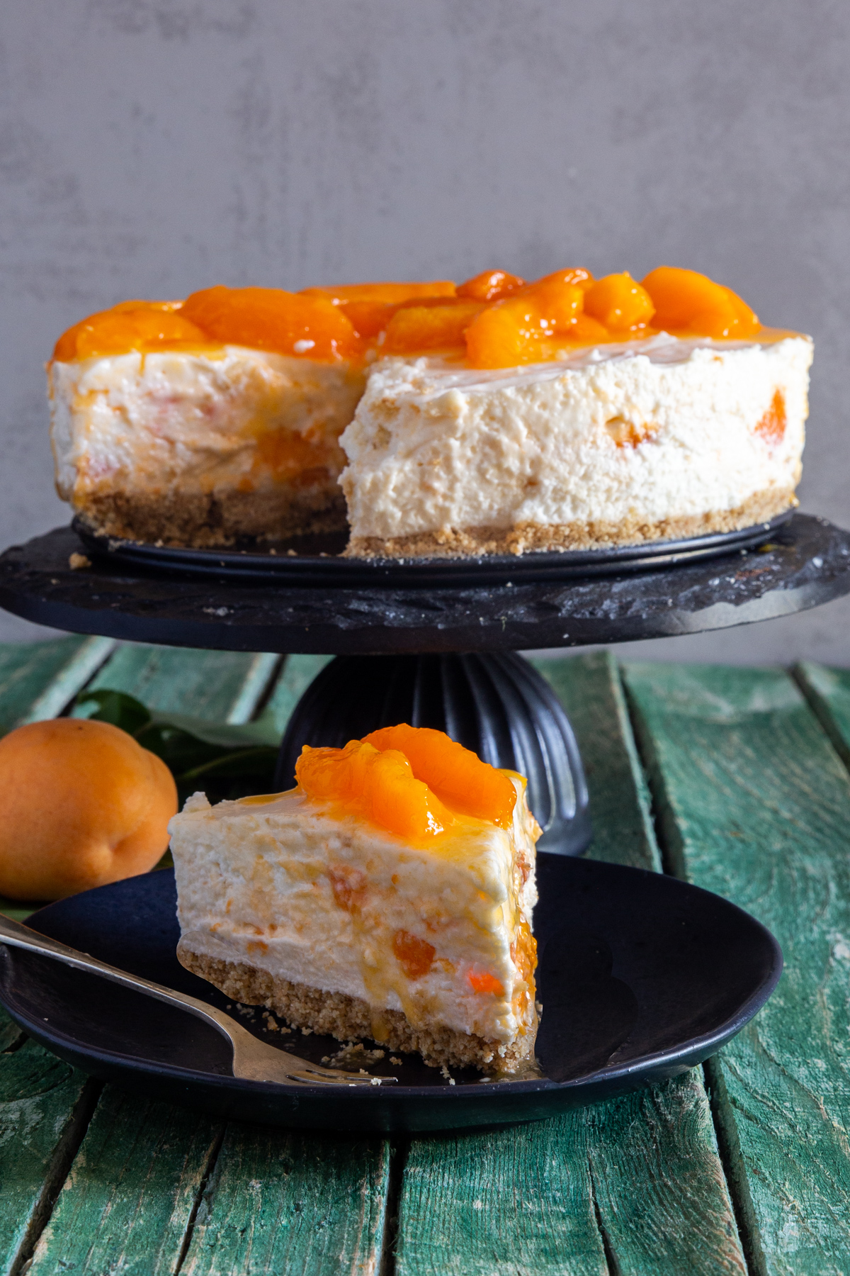 Cheesecake on a black cake stand with a slice on a black plate.