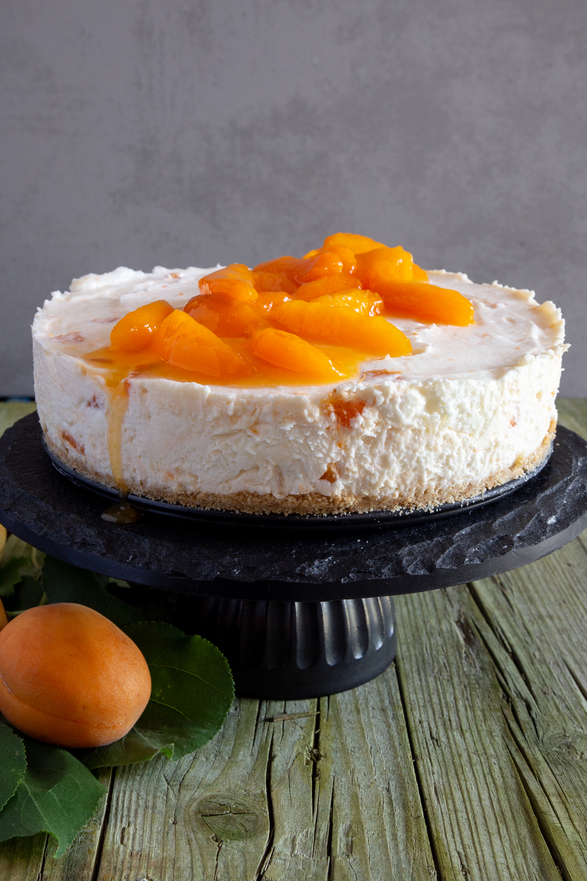 Apricot cheesecake on a black cake stand.