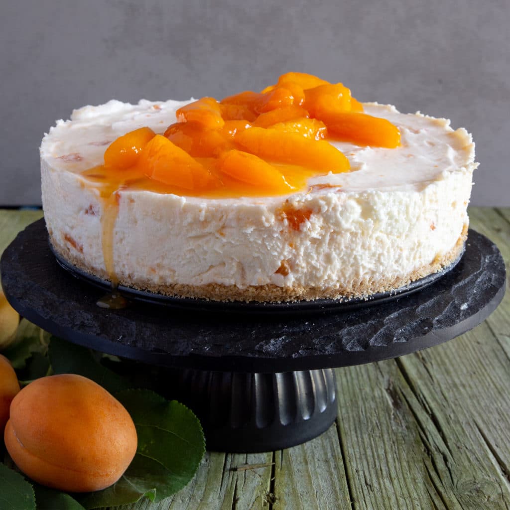 Apricot cheesecake on a black cake stand.