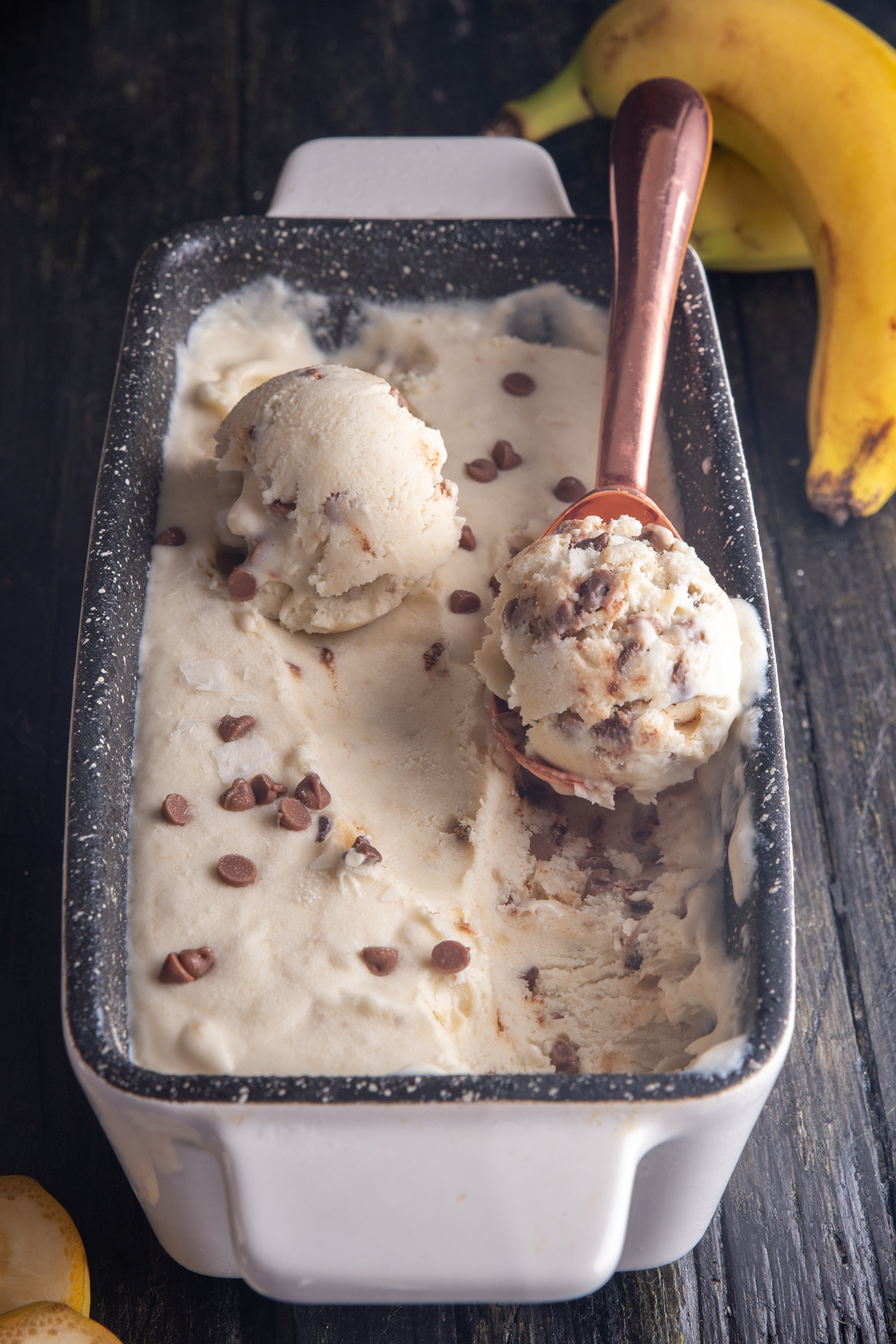 Banana ice cream in a white loaf pan with 2 scoops.