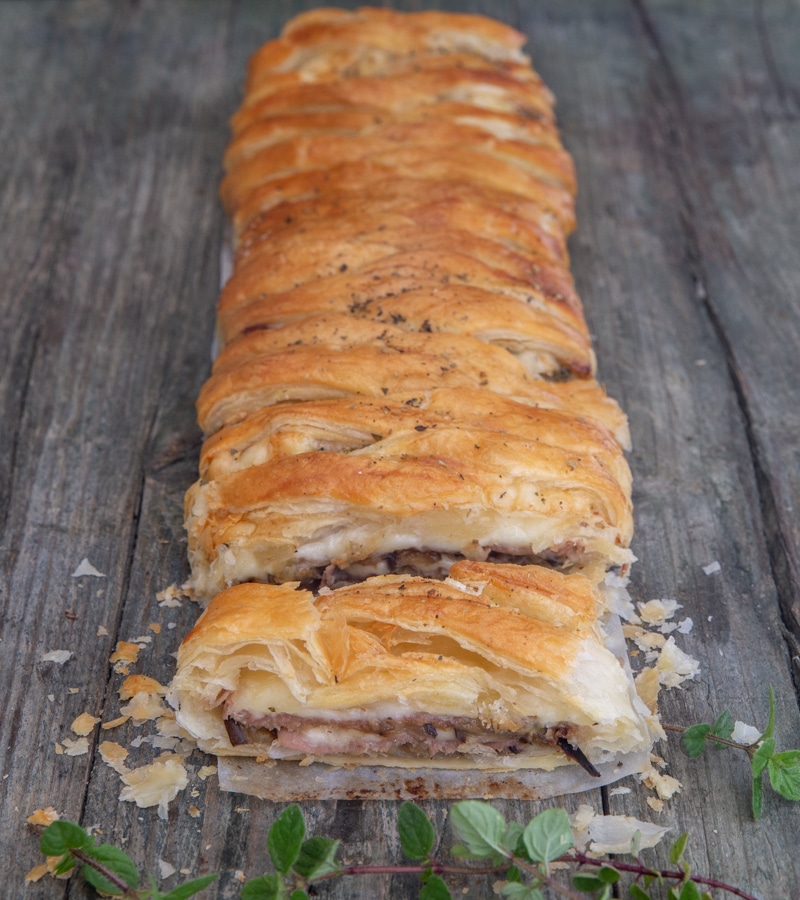 Eggplant strudel on a blue board with a slice cut.