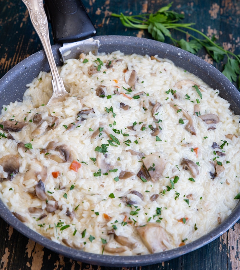 Mushroom risotto in a black pan with a silver spoon.