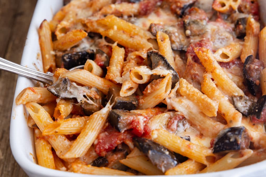 Sicilian pasta with some on a spoon in a white baking dish.