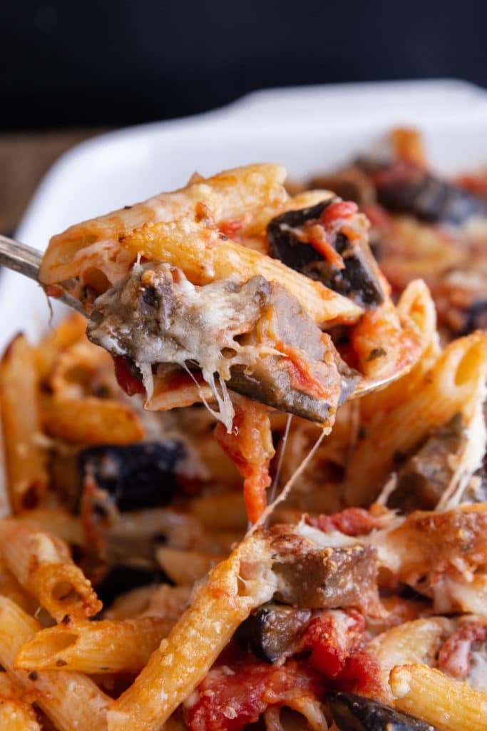 Pasta in a white baking dish with some on a spoon.