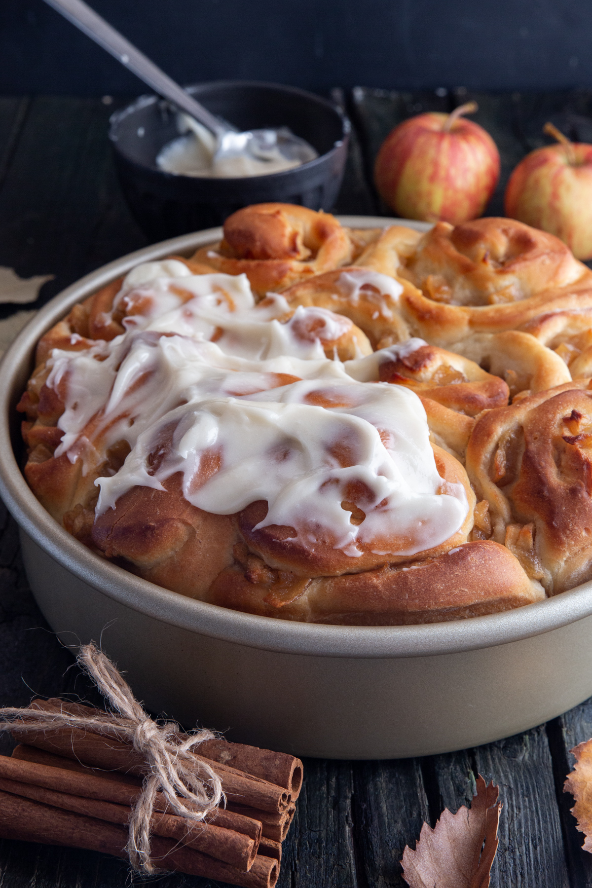 Apple cinnamon rolls with icing on top in a silver pan.