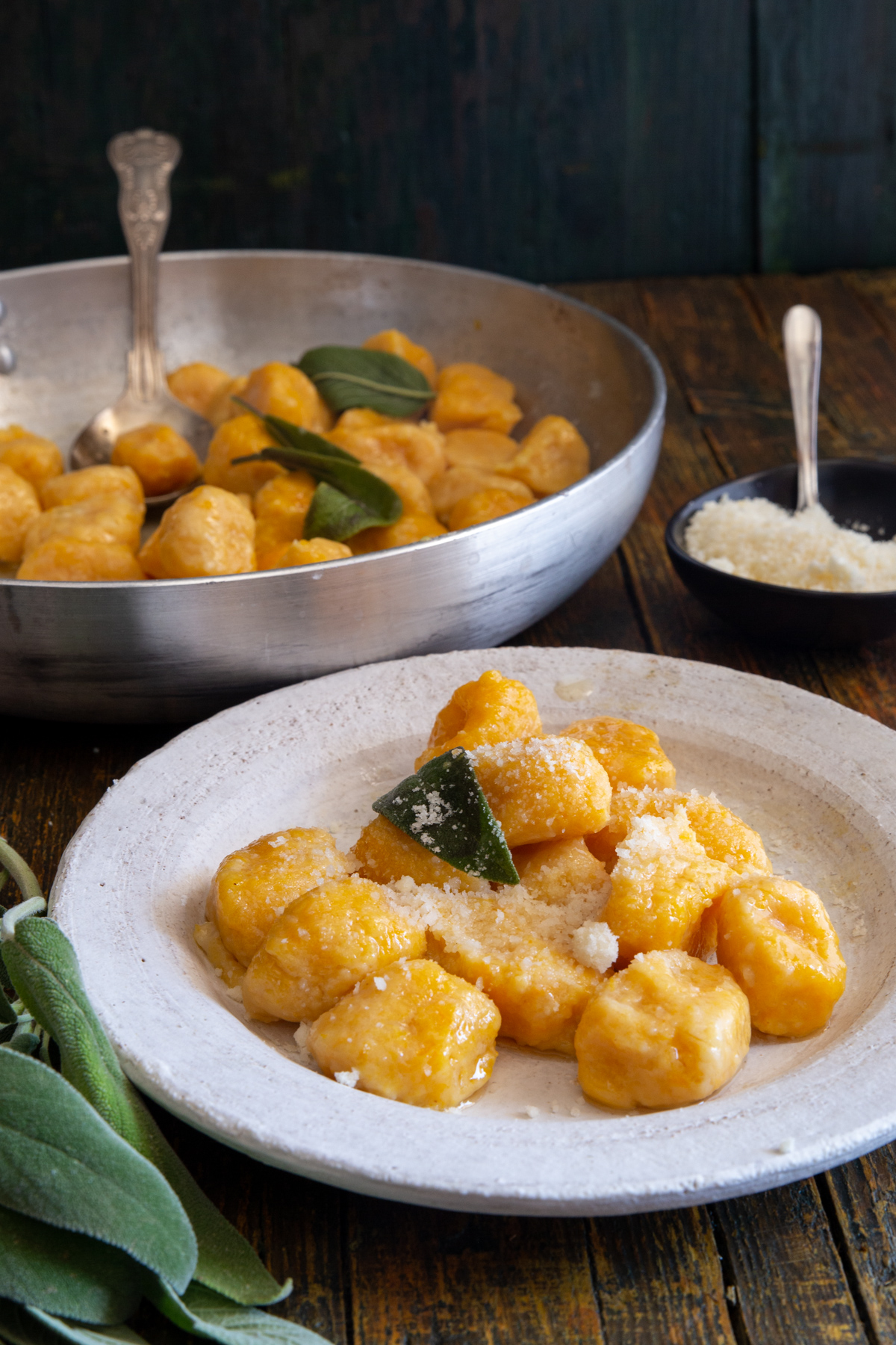 Pumpkin gnocchi in a white plate and some in a silver pan.