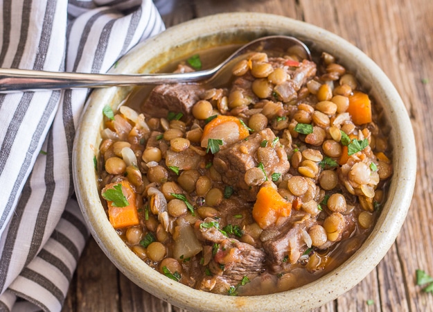 Beef and lentil stew in a brown bowl with a spoon.