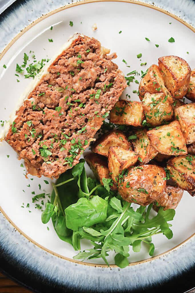 A slice of meatloaf on a white plate with salad and potatoes.