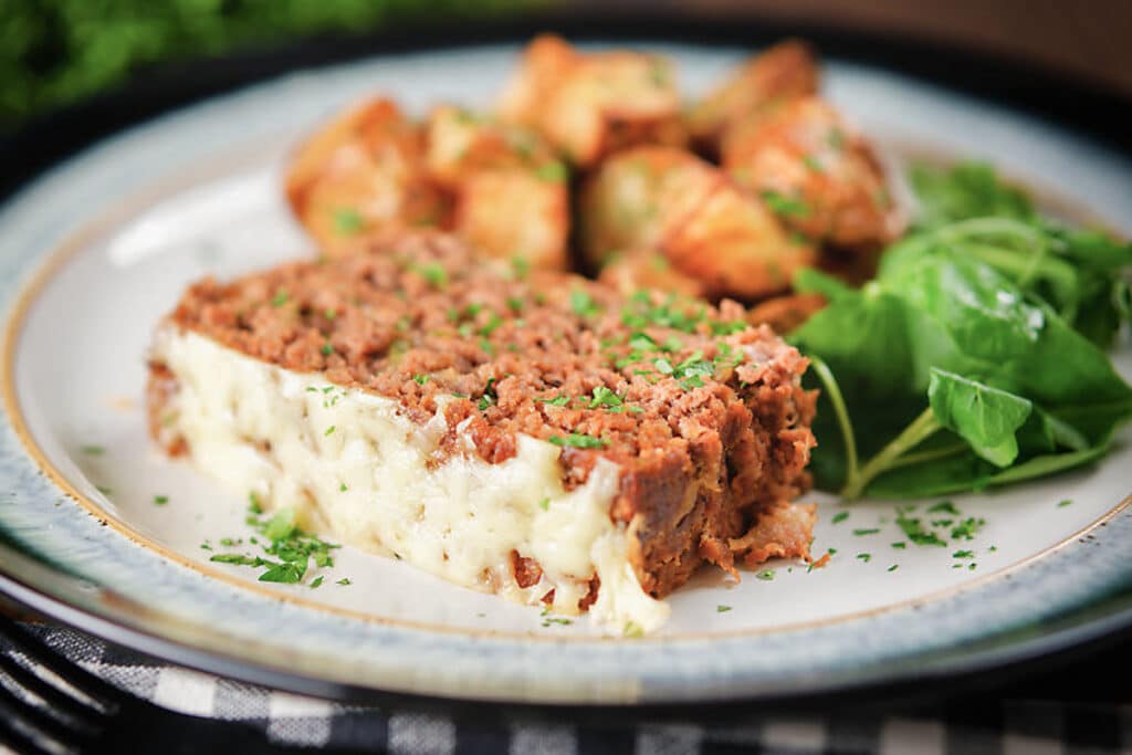 A slice of meatloaf on a white plate with salad and potatoes.