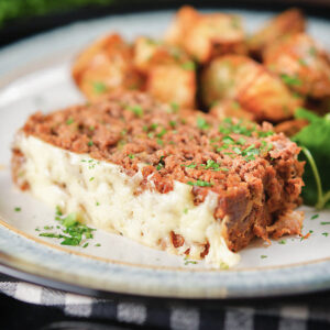 A slice of meatloaf on a white plate with salad and potatoes.