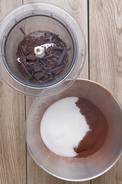 Chopped chocolate in a blender and ingredients in a silver bowl.