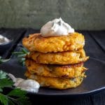 4 pumpkin fritters stacked on a black plate.