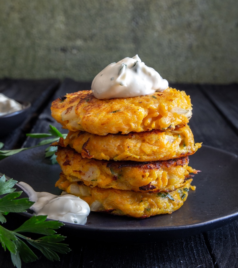 4 pumpkin fritters stacked on a black plate.