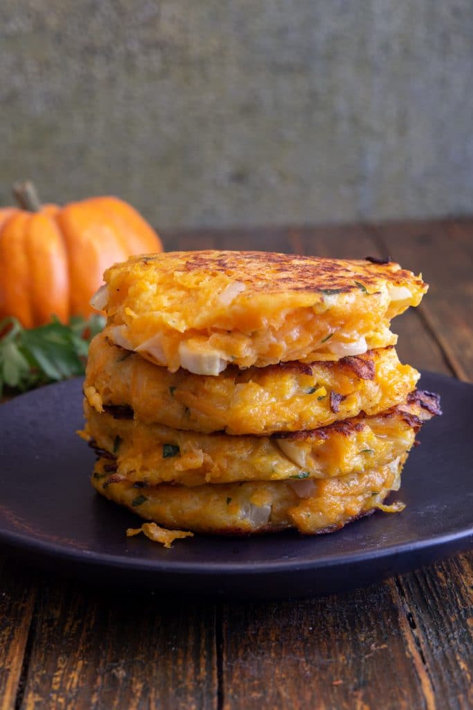 4 Pumpkin fritters stacked on a black plate.