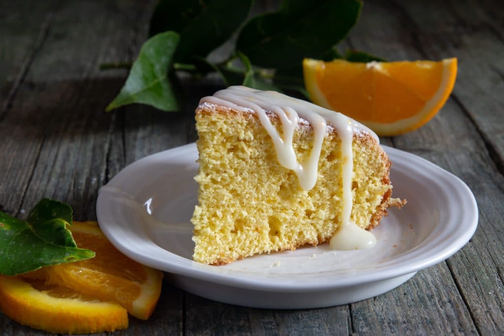 A slice of orange cake on a white plate drizzled with glaze.
