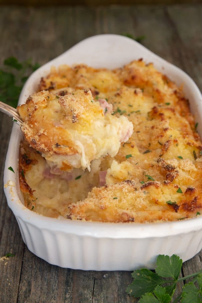 Potato casserole in a white dish with some on a spoon.