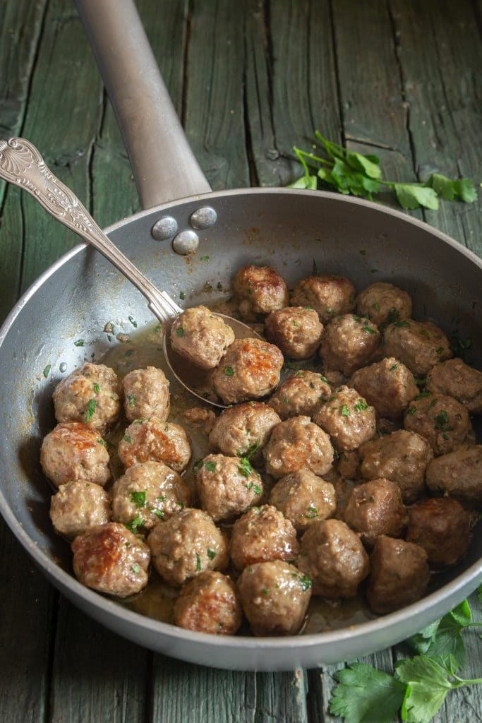 Meatballs in a silver frying pan with a spoon.