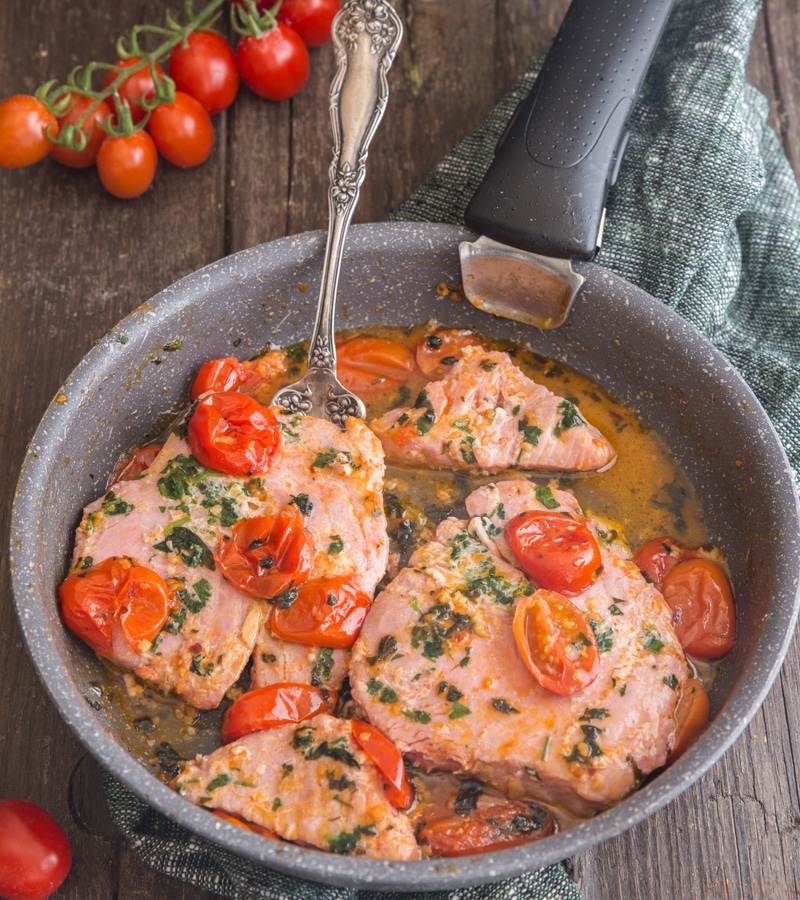 Tuna steaks with tomato in a frying pan.