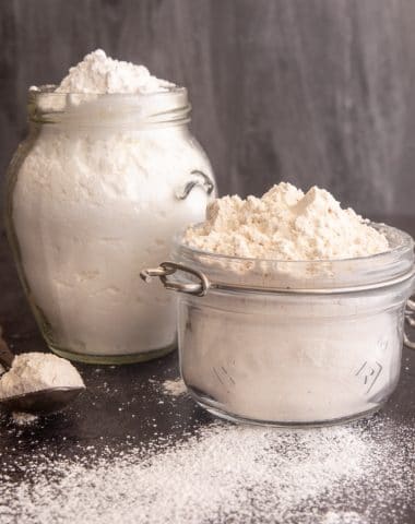 Brown and white powdered sugar in glass jars with some on a spoon.