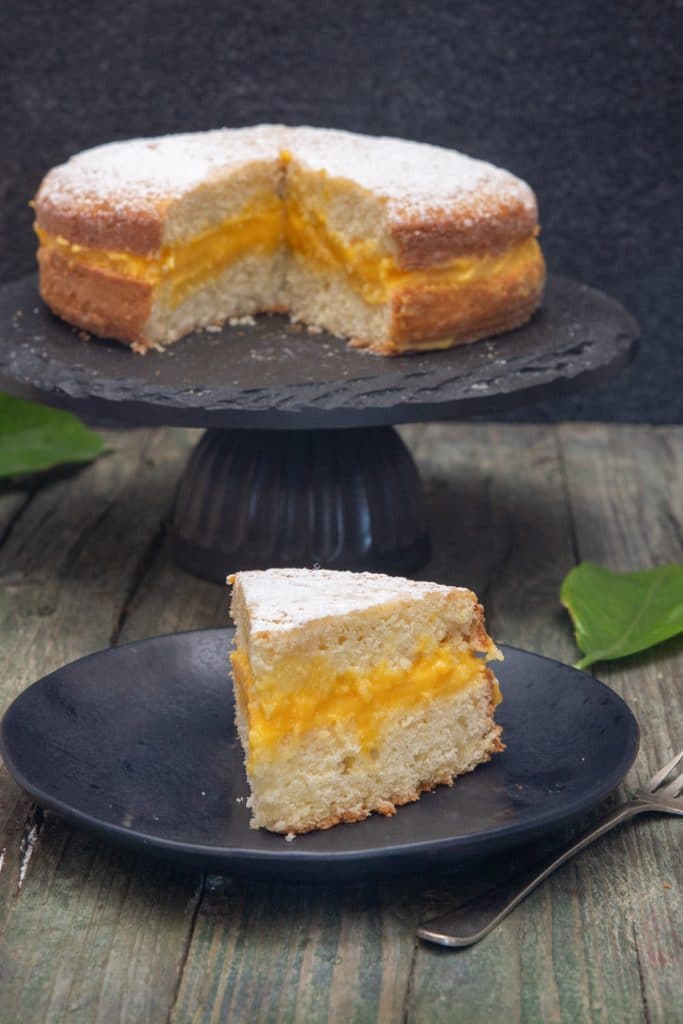 Lemon curd cake on a black plate stand with a slice on a black plate.