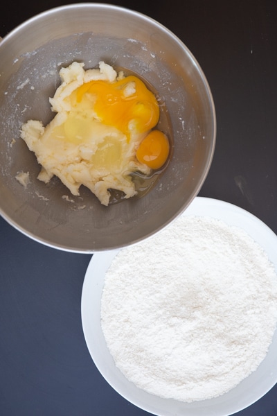 Whisking the flour in a white bowl and creamed butter and sugar with eggs added in mixing bowl.