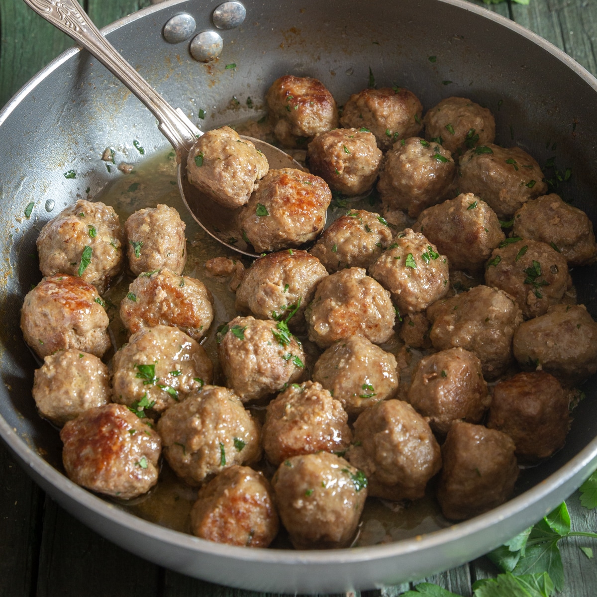 Meatballs in a silver frying pan with a spoon.