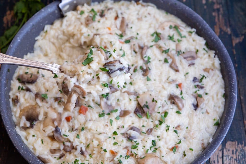 Mushroom risotto in a black pan with some on a spoon.