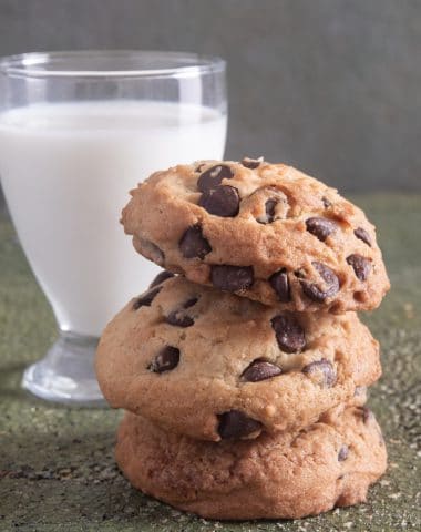 3 chocolate chip cookies stacked with a glass of milk.