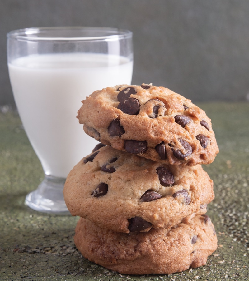 3 chocolate chip cookies stacked with a glass of milk.