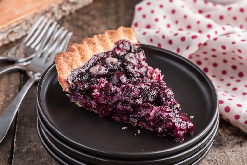 The blueberry pie slice on a black plate.