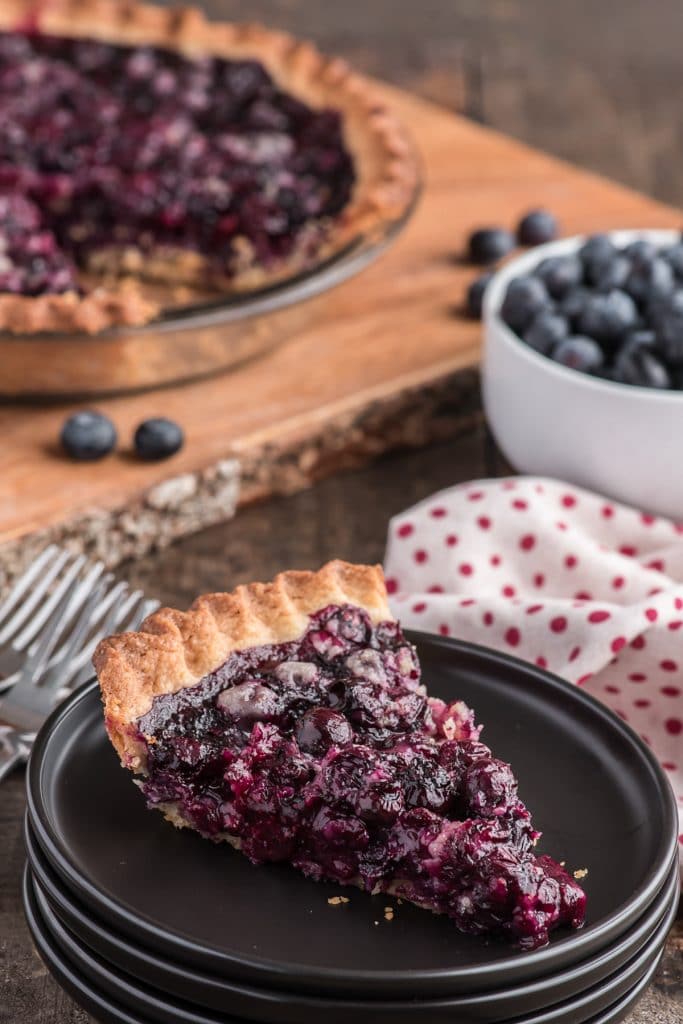 Blueberry pie with a slice on a black plate.