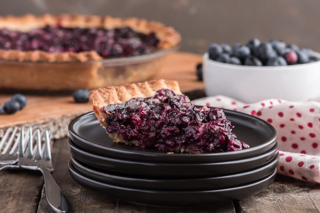 A slice of berry pie on a black plate.