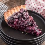 A slice of blueberry pie on a black plate.
