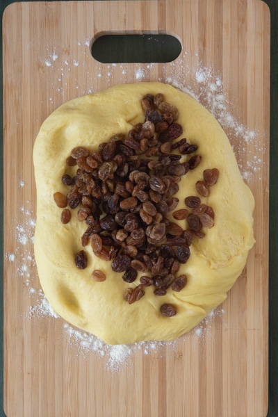 The dough on a board with raisins on top.