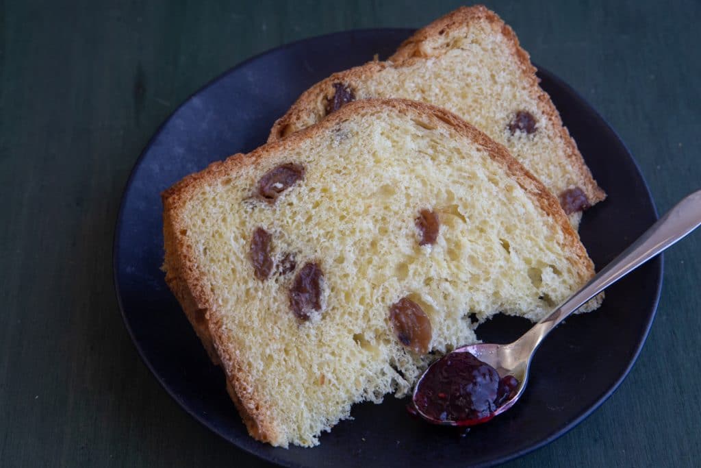 2 slices of easter bread on a black plate with a spoon of jam.
