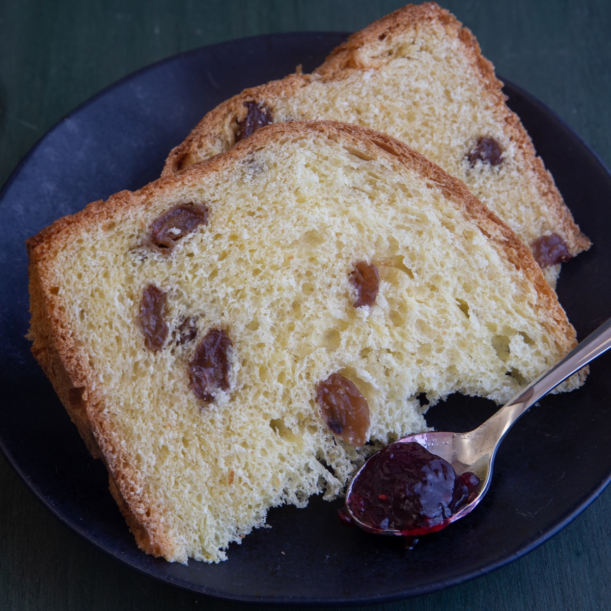 2 slices of easter bread on a black plate with a spoon of jam.